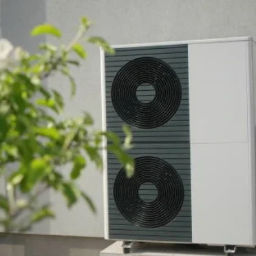 Weiße Wärmepumpe  vor einer Wand und grünen Pflanzen