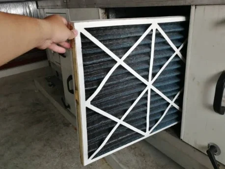 Eine Hand hält einen verschutzten Luftfilter, der gerade aus einer Lüftungsanlage entnommen wird.